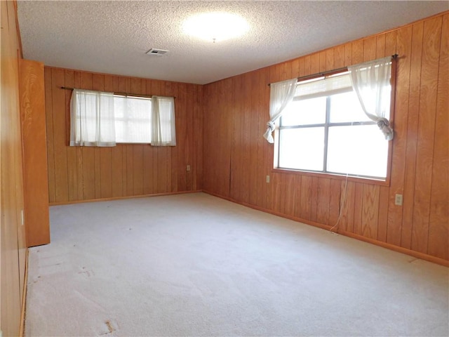 spare room featuring carpet, visible vents, wooden walls, a textured ceiling, and baseboards