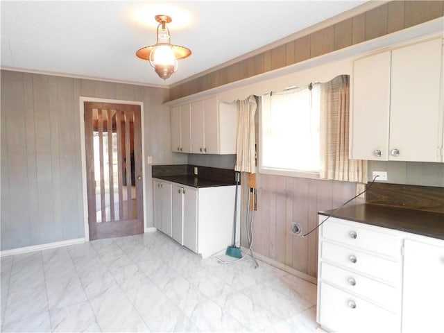 kitchen with dark countertops, ornamental molding, marble finish floor, wood walls, and white cabinetry