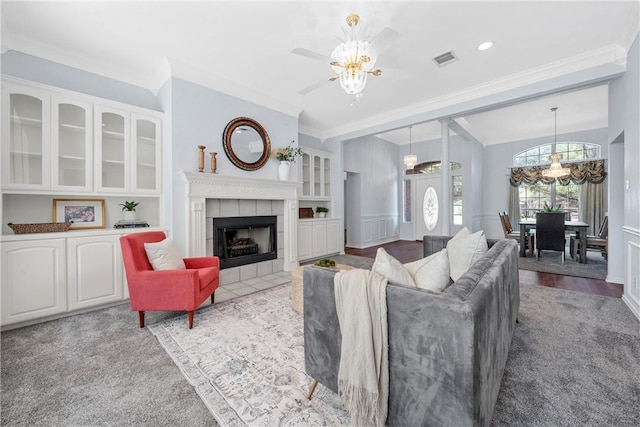 living room with ceiling fan with notable chandelier, vaulted ceiling, ornamental molding, light colored carpet, and a tiled fireplace