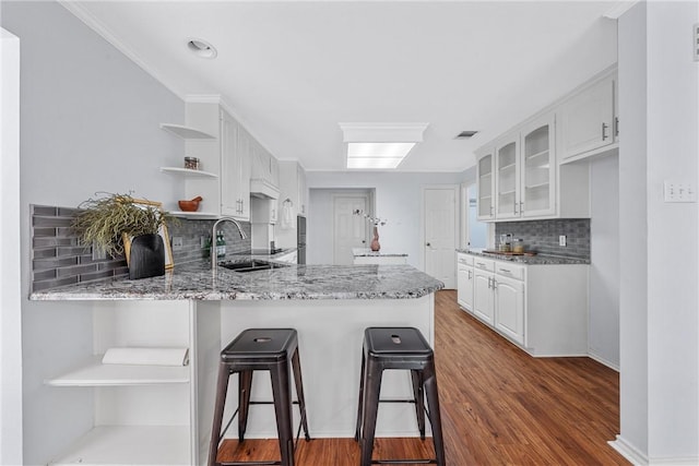 kitchen with white cabinetry, wood-type flooring, kitchen peninsula, and sink