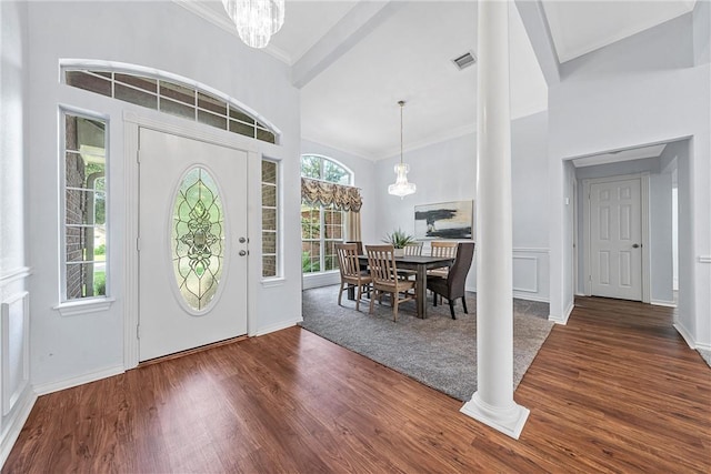 entryway with dark hardwood / wood-style flooring, ornate columns, ornamental molding, an inviting chandelier, and a high ceiling