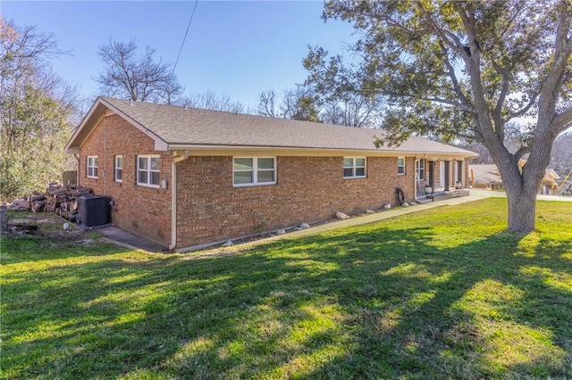 rear view of property with a yard, a shingled roof, central AC, and brick siding