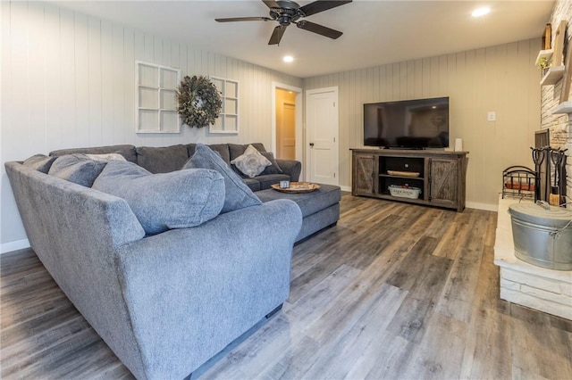 living room featuring dark wood-type flooring, a large fireplace, and ceiling fan