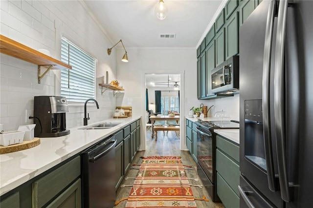 kitchen with sink, green cabinetry, crown molding, appliances with stainless steel finishes, and hardwood / wood-style flooring