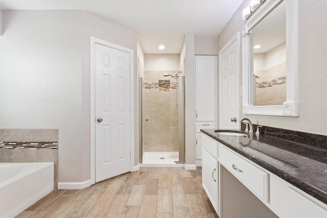 bathroom with wood finished floors, vanity, baseboards, a shower stall, and a bath