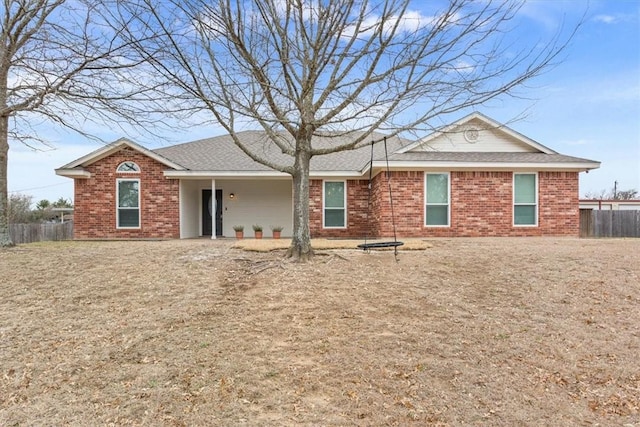 view of front of property featuring brick siding, fence, and roof with shingles