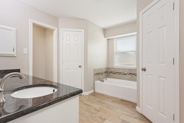 full bath with a garden tub, vanity, baseboards, and wood finished floors