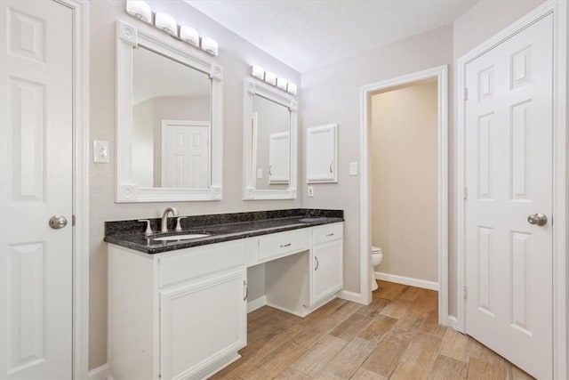 bathroom featuring toilet, baseboards, wood finished floors, and vanity