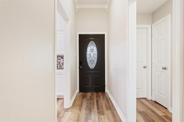 doorway with light wood-style floors, ornamental molding, and baseboards