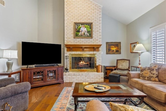 living room featuring wood-type flooring, vaulted ceiling, and a brick fireplace