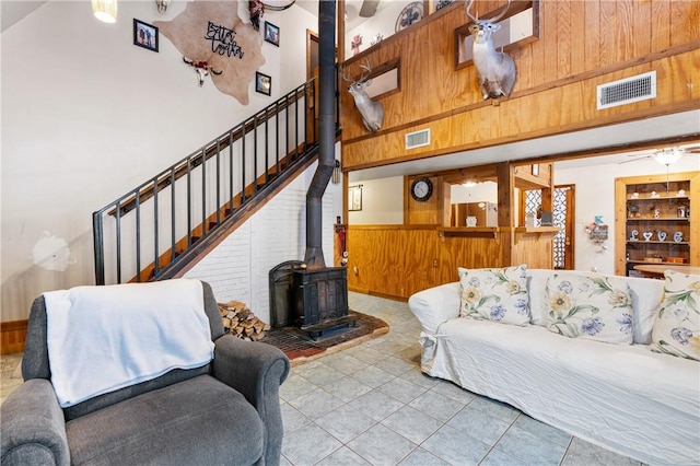 living room featuring a wood stove, wooden walls, a towering ceiling, and light tile patterned floors