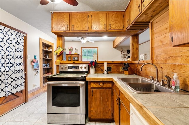 kitchen with stainless steel electric stove, tile countertops, wooden walls, and sink