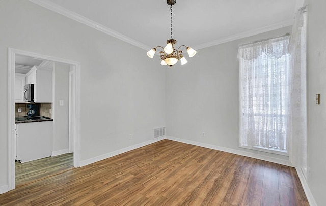 unfurnished dining area featuring visible vents, a healthy amount of sunlight, crown molding, wood finished floors, and a notable chandelier