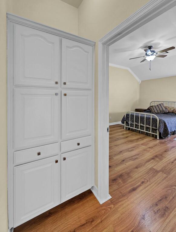 bedroom with wood finished floors, baseboards, ornamental molding, vaulted ceiling, and a closet