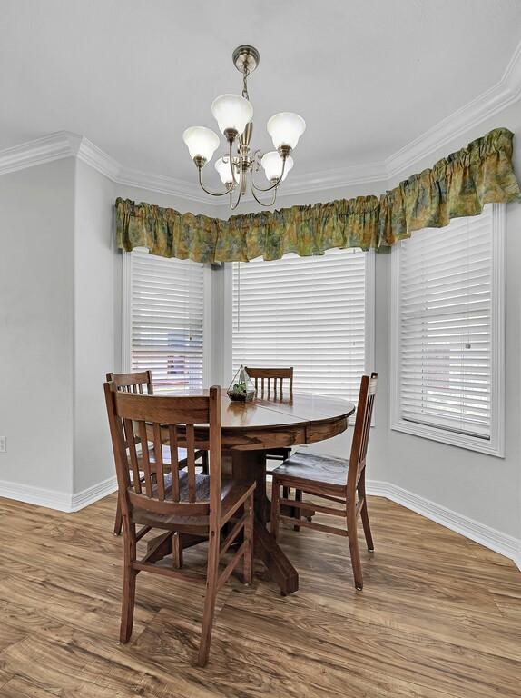 dining room with an inviting chandelier, wood finished floors, crown molding, and baseboards