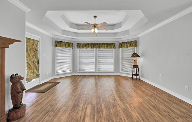 spare room featuring crown molding, baseboards, wood finished floors, a raised ceiling, and a ceiling fan