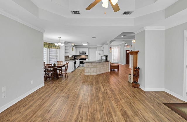 living area with arched walkways, visible vents, ceiling fan with notable chandelier, and a tray ceiling