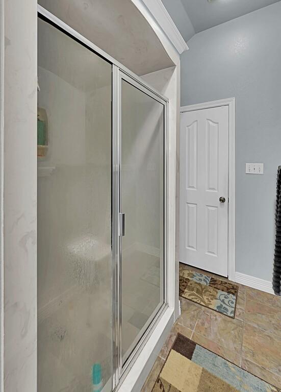 bathroom with a shower stall, stone tile floors, and baseboards