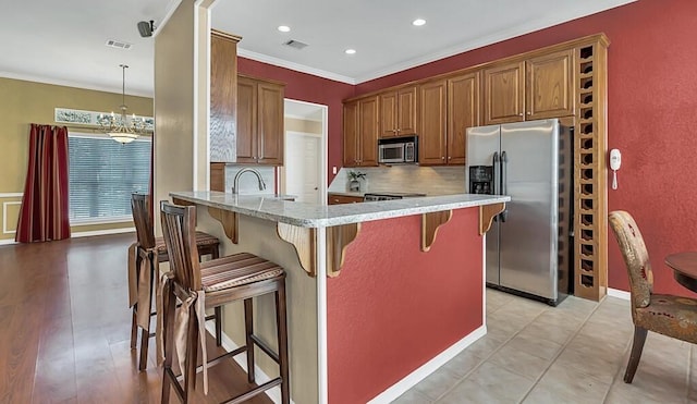 kitchen featuring light stone countertops, kitchen peninsula, backsplash, stainless steel appliances, and hanging light fixtures