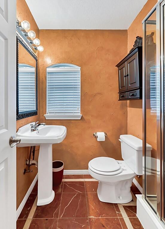 bathroom featuring toilet, a shower with shower door, and sink