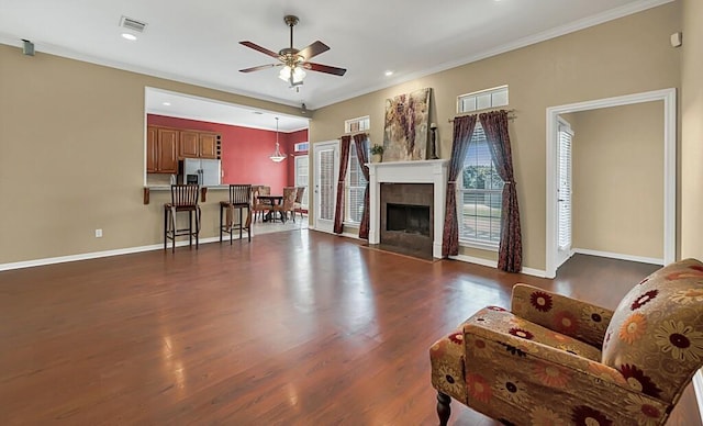 living room featuring a fireplace, ceiling fan, crown molding, and dark wood-type flooring