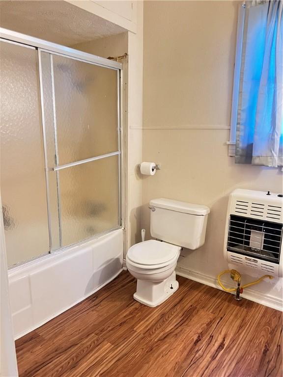 bathroom featuring heating unit, hardwood / wood-style floors, enclosed tub / shower combo, and toilet