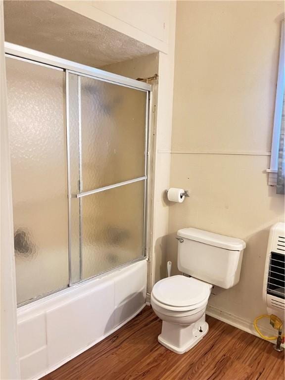 bathroom featuring toilet, wood-type flooring, bath / shower combo with glass door, and heating unit