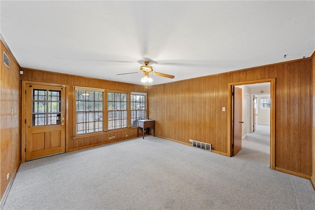 spare room with ceiling fan, wooden walls, and light colored carpet