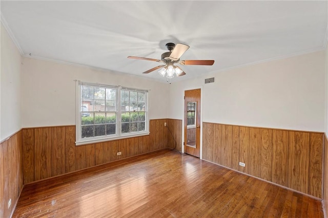 spare room with wooden walls, hardwood / wood-style floors, ceiling fan, and ornamental molding