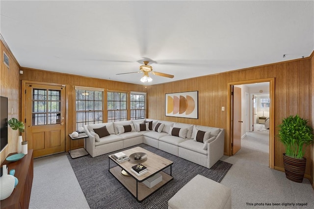 carpeted living room featuring crown molding, ceiling fan, and wooden walls