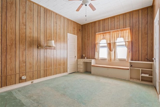 carpeted spare room with ceiling fan, wooden walls, and built in desk