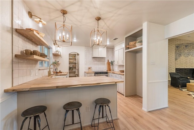 kitchen with wood counters, white cabinets, sink, kitchen peninsula, and a breakfast bar area