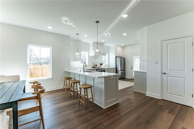 kitchen with kitchen peninsula, stainless steel fridge, dark wood-type flooring, and hanging light fixtures