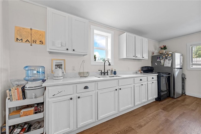 kitchen featuring stainless steel refrigerator, sink, black range with electric cooktop, white cabinets, and light wood-type flooring