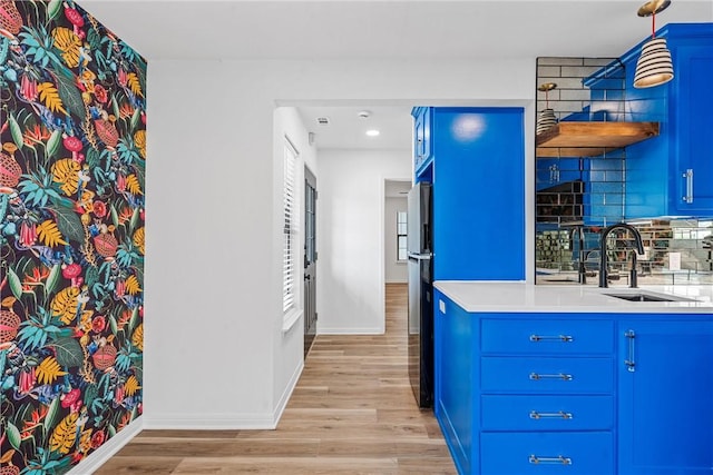 kitchen featuring blue cabinets, sink, decorative backsplash, light wood-type flooring, and decorative light fixtures