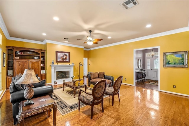 living room featuring light wood-type flooring, ceiling fan with notable chandelier, built in features, and ornamental molding