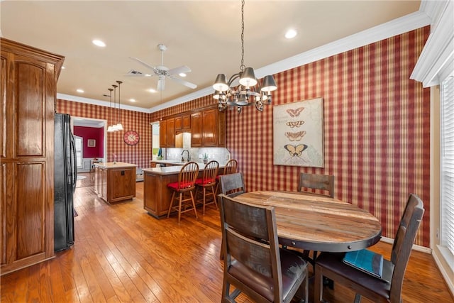 dining area with sink, light hardwood / wood-style floors, ceiling fan with notable chandelier, and ornamental molding