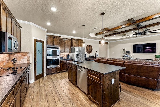 kitchen featuring hanging light fixtures, beamed ceiling, decorative backsplash, a center island with sink, and appliances with stainless steel finishes