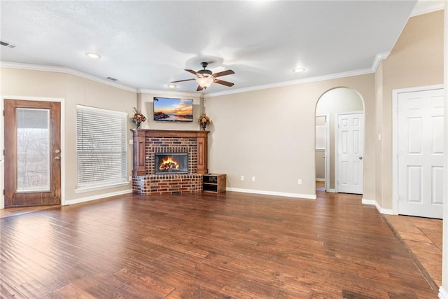 unfurnished living room featuring a brick fireplace, crown molding, arched walkways, and wood finished floors