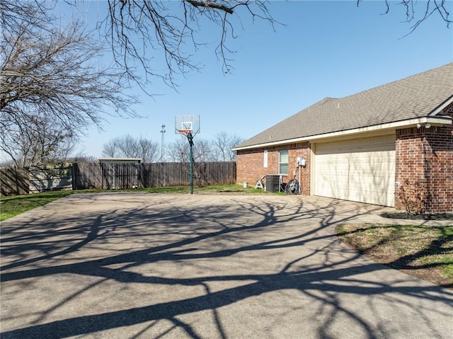 view of home's exterior with brick siding, a shingled roof, fence, a garage, and driveway