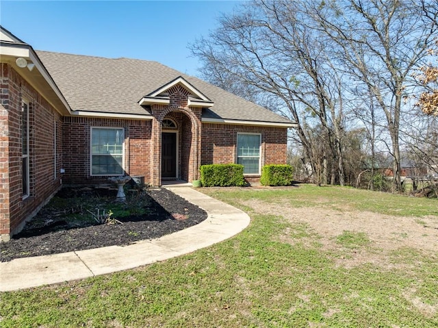 view of front of house with brick siding, roof with shingles, and a front yard