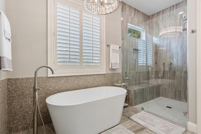 bathroom with an inviting chandelier, shower with separate bathtub, and tile walls