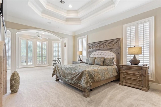 carpeted bedroom featuring a raised ceiling, ornamental molding, multiple windows, and ornate columns