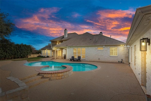 pool at dusk with a patio and an in ground hot tub