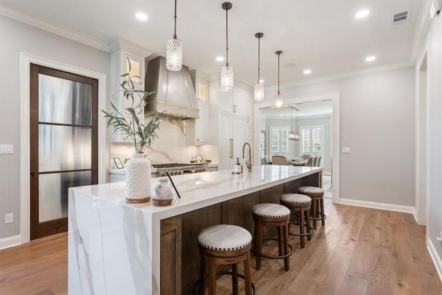 kitchen with white cabinetry, light hardwood / wood-style floors, a spacious island, hanging light fixtures, and custom range hood