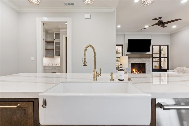 kitchen with light stone countertops, sink, a stone fireplace, and ornamental molding