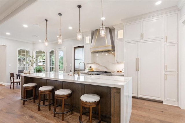 kitchen with white cabinetry, premium range hood, hanging light fixtures, and an island with sink