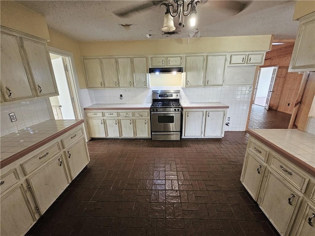 kitchen featuring tile countertops, a textured ceiling, backsplash, and gas range