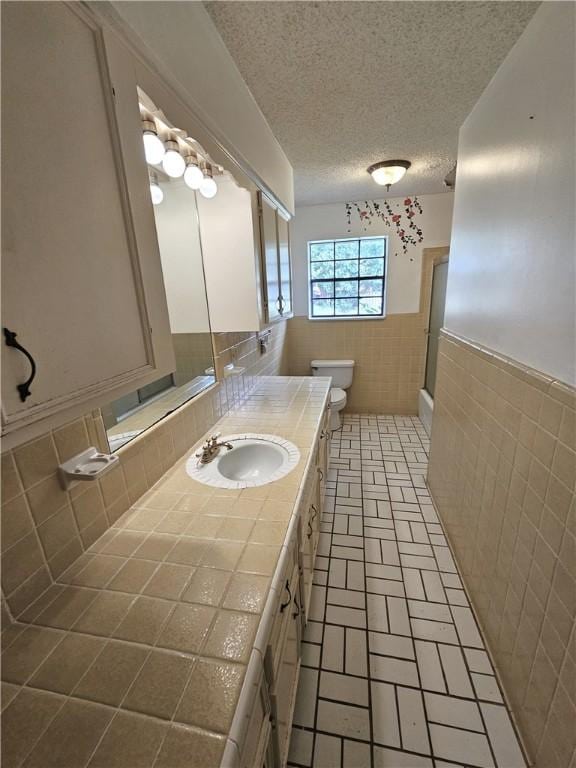 bathroom with a textured ceiling, toilet, vanity, a shower with shower door, and tile walls