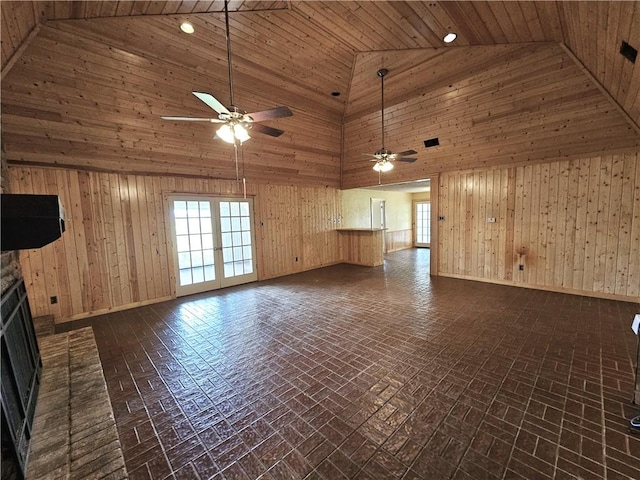 unfurnished living room with ceiling fan, wooden walls, high vaulted ceiling, and a brick fireplace